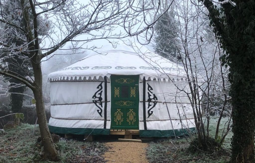 Exterior view of a traditional whit Mongolian yurt with green door set in a natural woodland setting, ideal for glamping or retreat use