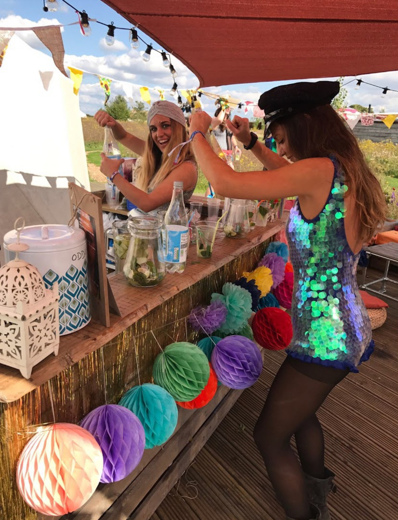 Two woman in festive outfits serving drinks at a decorated outdoor bar.