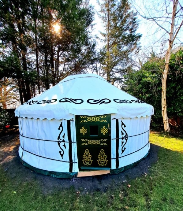 Exterior view of a traditional white canvas yurt with green ornamental door set in a lush forest clearing