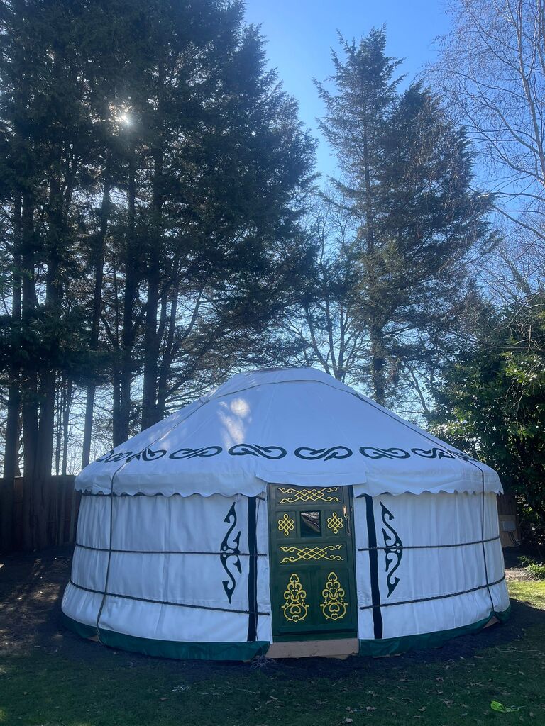 White glamping yurt forest setting - Visit our Oxford Show yurt or Speak to Us Exterior view of a traditional white canvas yurt with green ornamental door set in a lush forest clearing