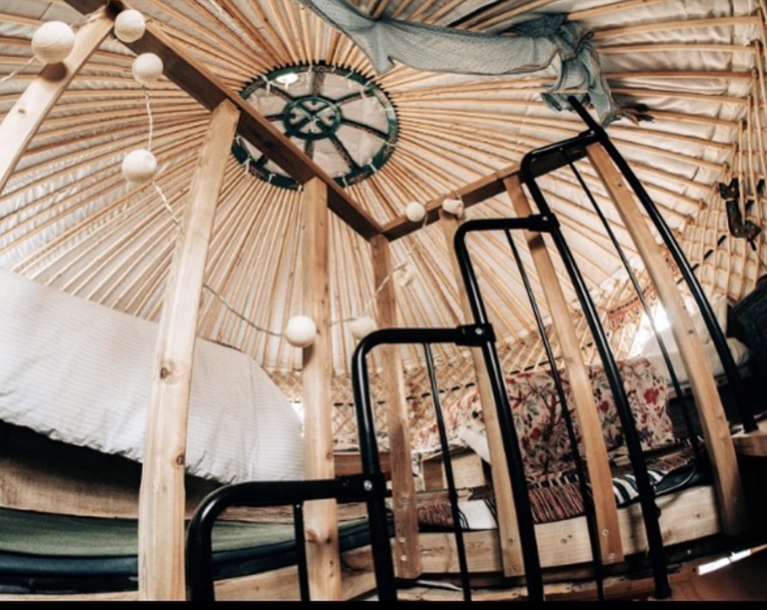 Hapus Yurt | Yurt interior Ceiling and Loft - Welcome to Yurt Specialists Interior of a wooden-domed ceiling with radial beams and a central circular green roof crown feature, foreground shows black metal railing.