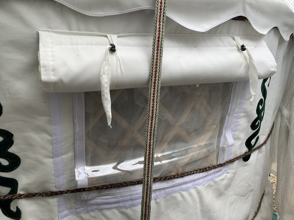 Close-up of a weather-resistant while Mongolian yurt wall canvas featuring an open able window flap with a clear PVC screen, mosquito netting, and insulated cover.