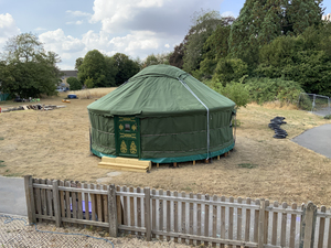 Green Mongolian Yurt Pitched On-Site - Welcome to Yurt Specialists Green traditional Mongolian yurt with decorative wooden door pitched in an outdoors school ground surrounded by trees and playground equipment.
